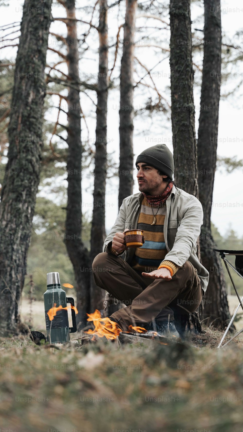 a man sitting next to a fire in a forest