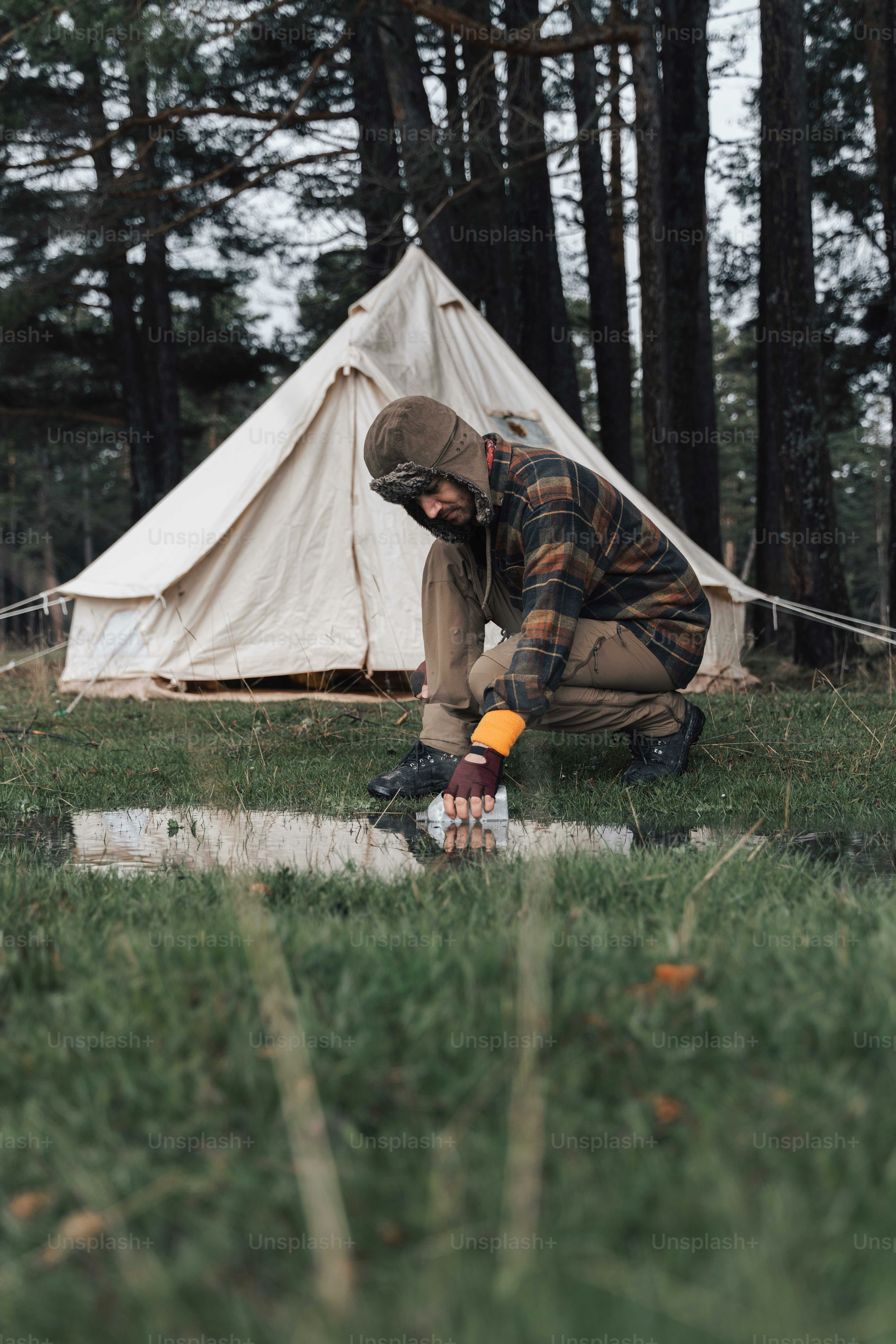 a man kneeling down in the grass next to a tent