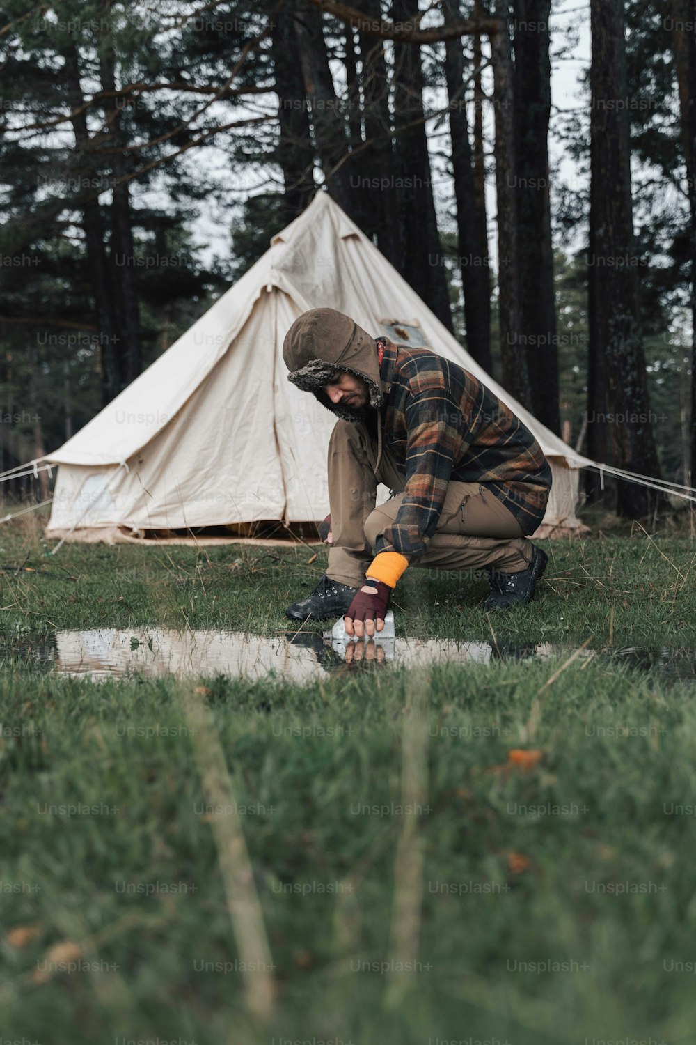 um homem ajoelhado na grama ao lado de uma tenda