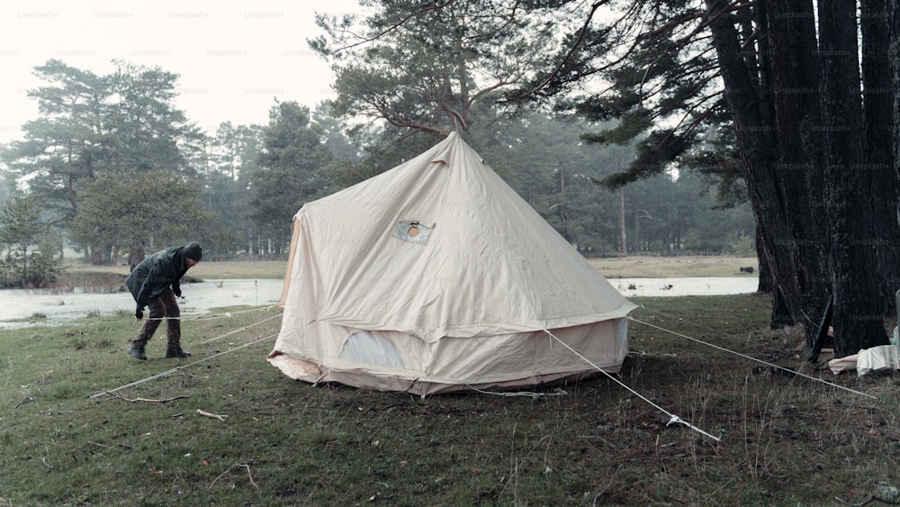 a man standing next to a tent in a forest