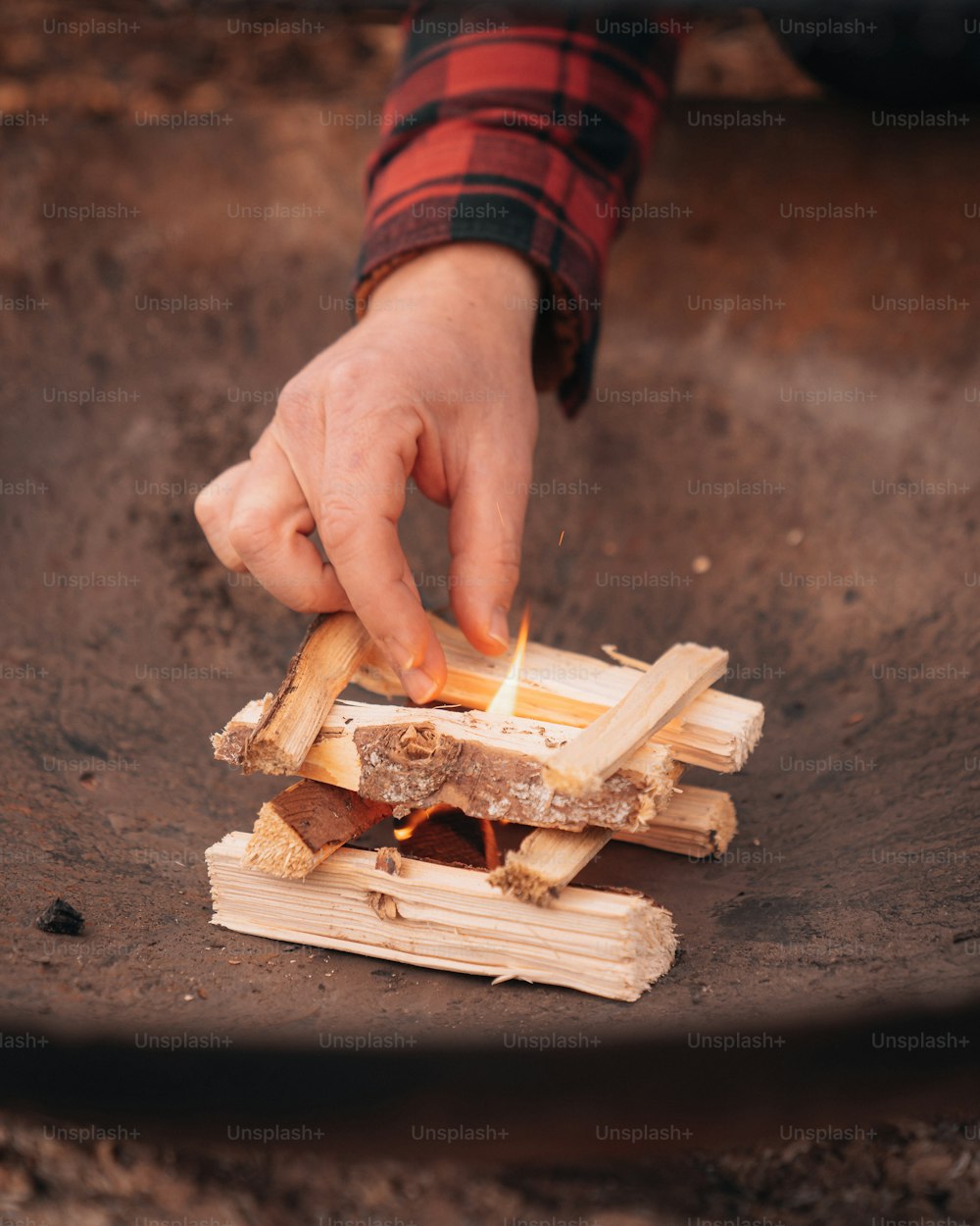 a person holding a lit match over a pile of wood