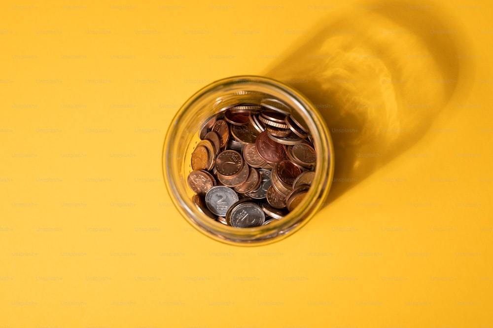 un barattolo pieno di monete seduto in cima a un tavolo giallo