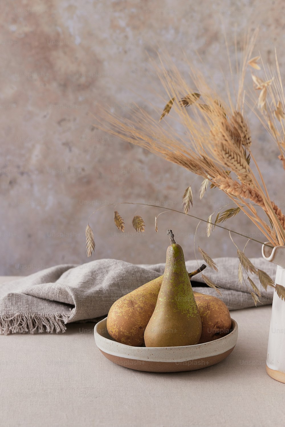a bowl of pears and some wheat on a table