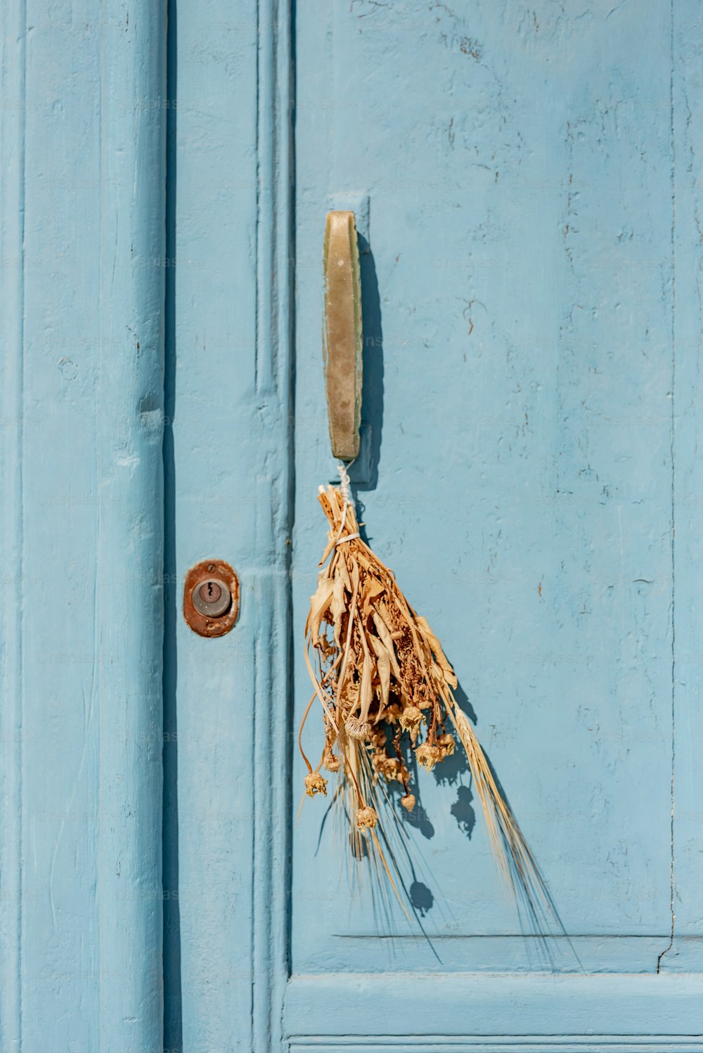 Eine blaue Tür, an der ein Strauß getrockneter Blumen hängt