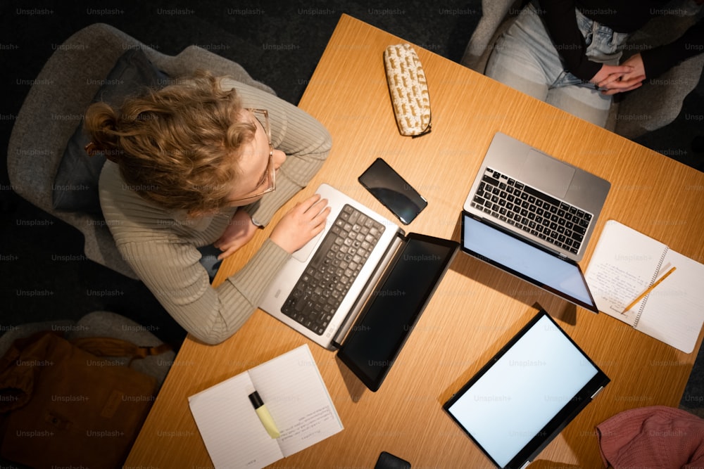 a woman sitting at a table with two laptops