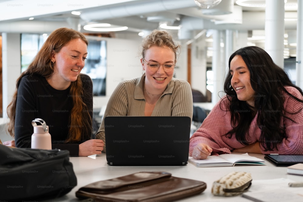 three women sitting at a table looking at a laptop