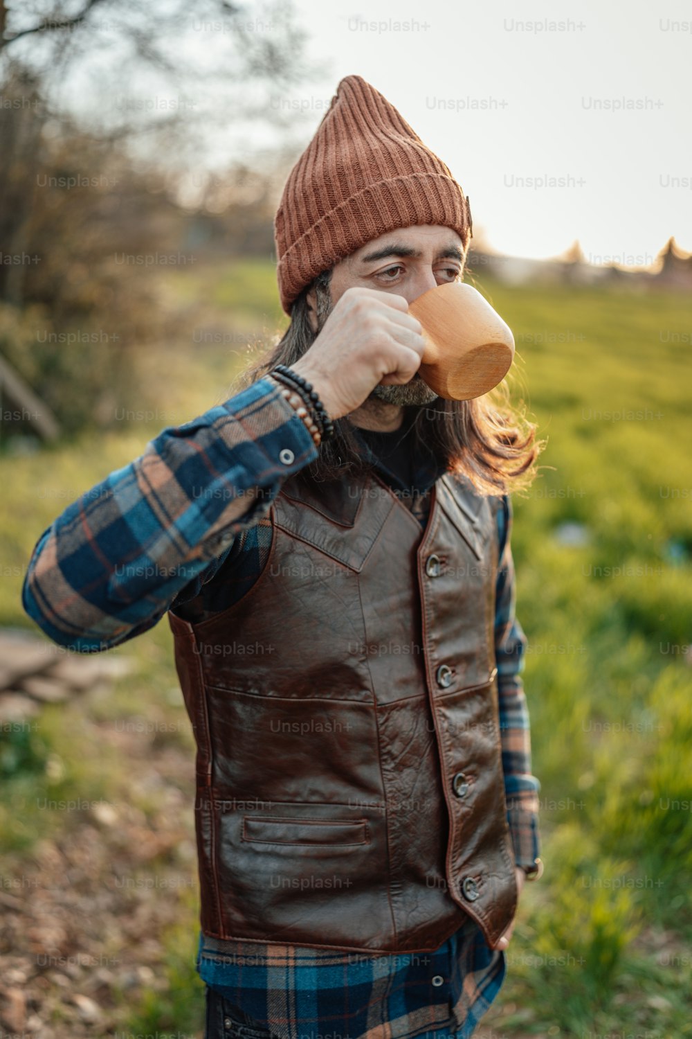 Un uomo con una camicia a quadri e un cappello marrone che beve una tazza di caffè