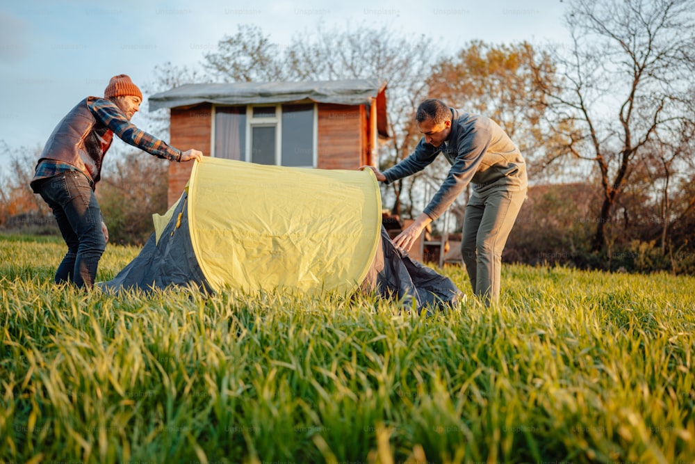 Zwei Personen, die ein Zelt auf einem Feld aufstellen