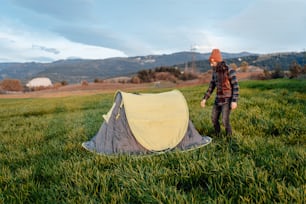 a man standing next to a tent in a field