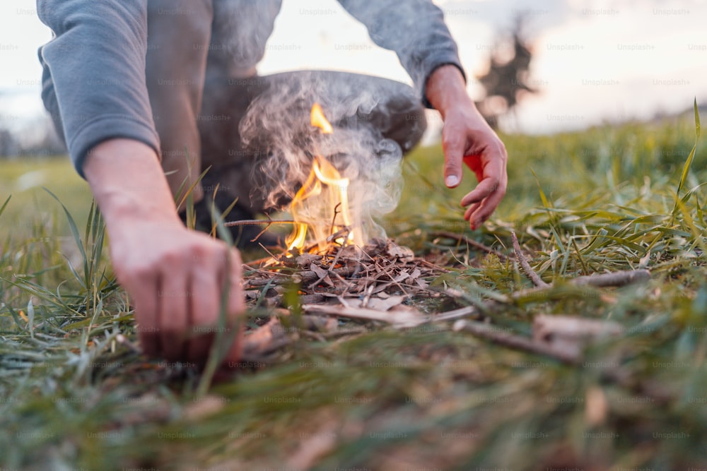 a person kneeling down next to a fire in the grass