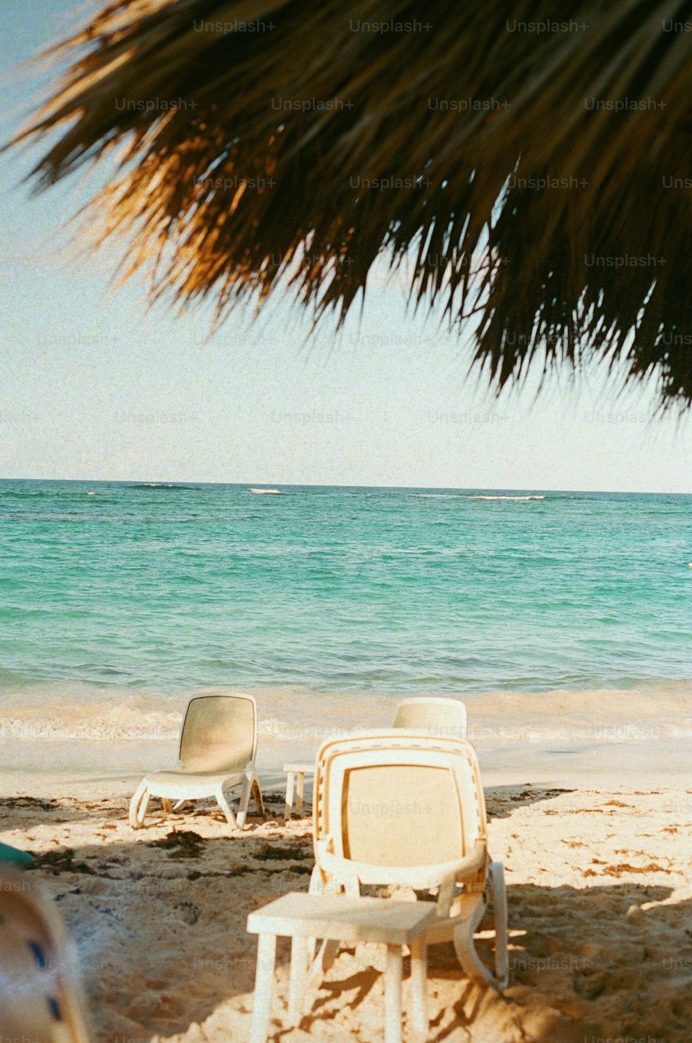 uma praia com cadeiras e um guarda-sol de palha