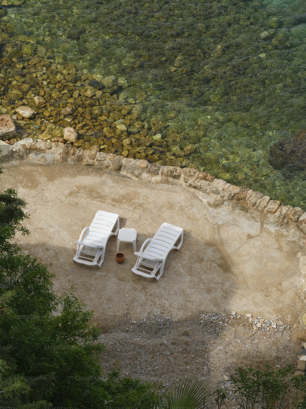 Dos sillas blancas de jardín sentadas encima de un campo de tierra