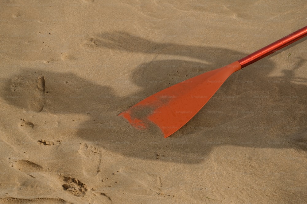 a red paddle sitting on top of a sandy beach