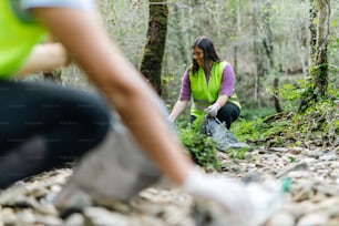 a woman in a green vest is picking up trash in the woods