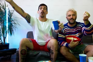 two men sitting on a couch eating popcorn