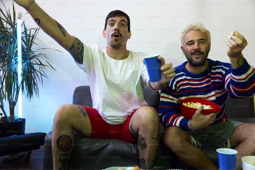 two men sitting on a couch eating popcorn