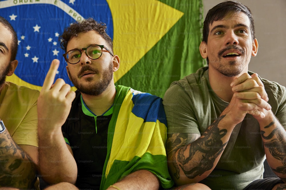 três homens sentados um ao lado do outro em frente a uma bandeira