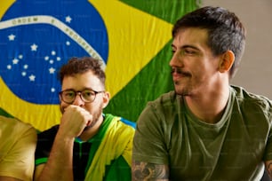 two men sitting next to each other in front of a flag