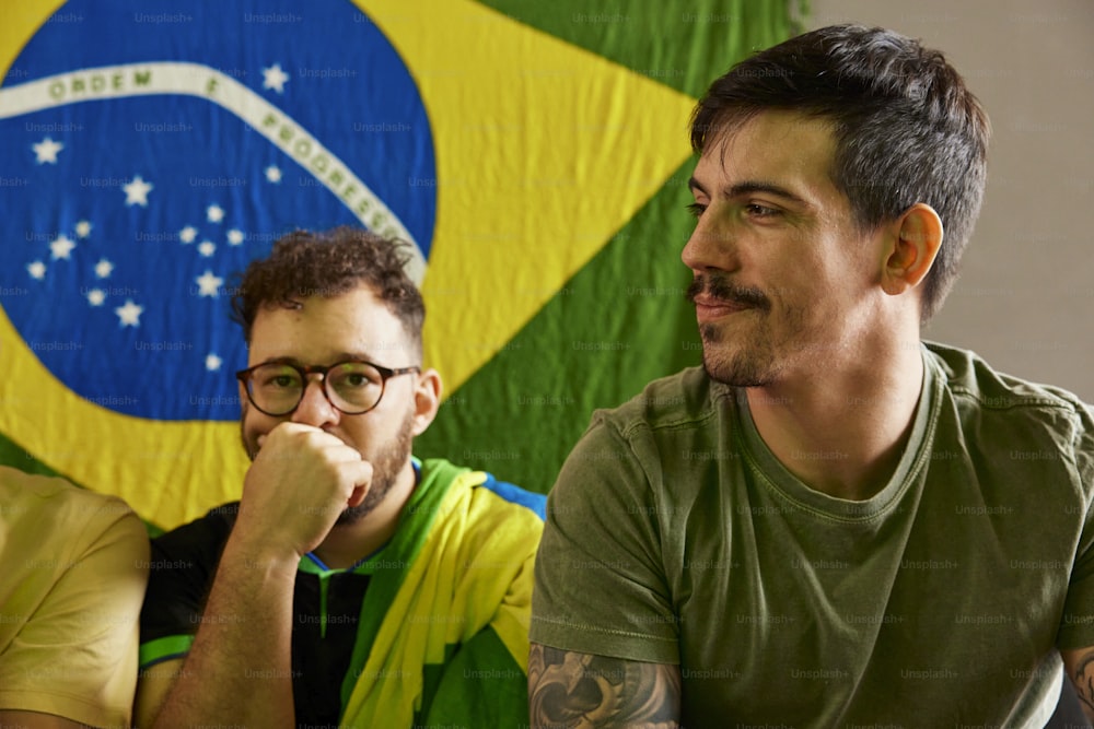 two men sitting next to each other in front of a flag