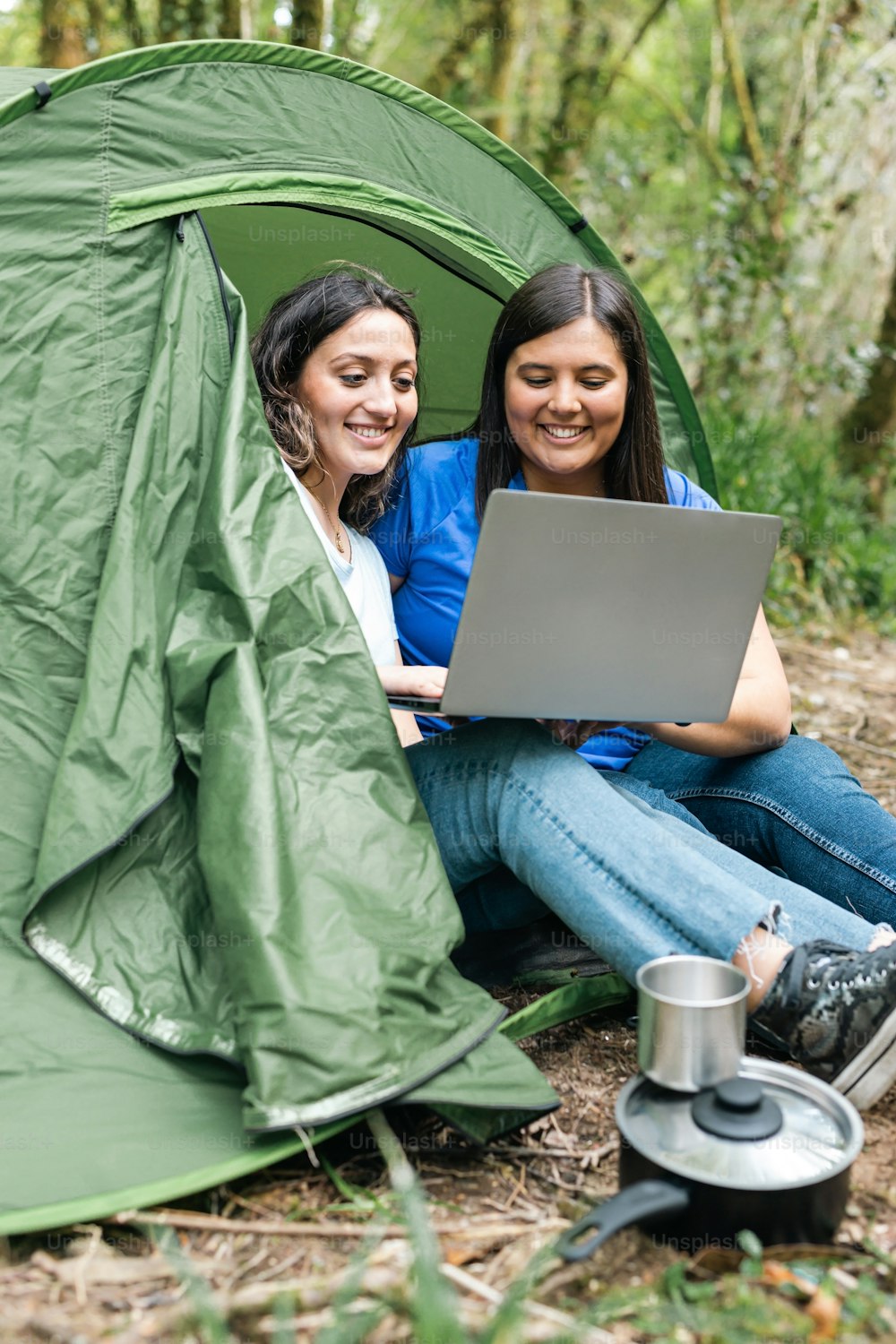 two women sitting in a tent with a laptop