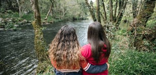 two girls are looking at a river in the woods