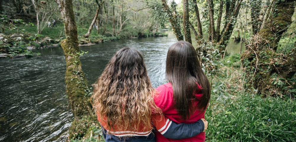two girls are looking at a river in the woods