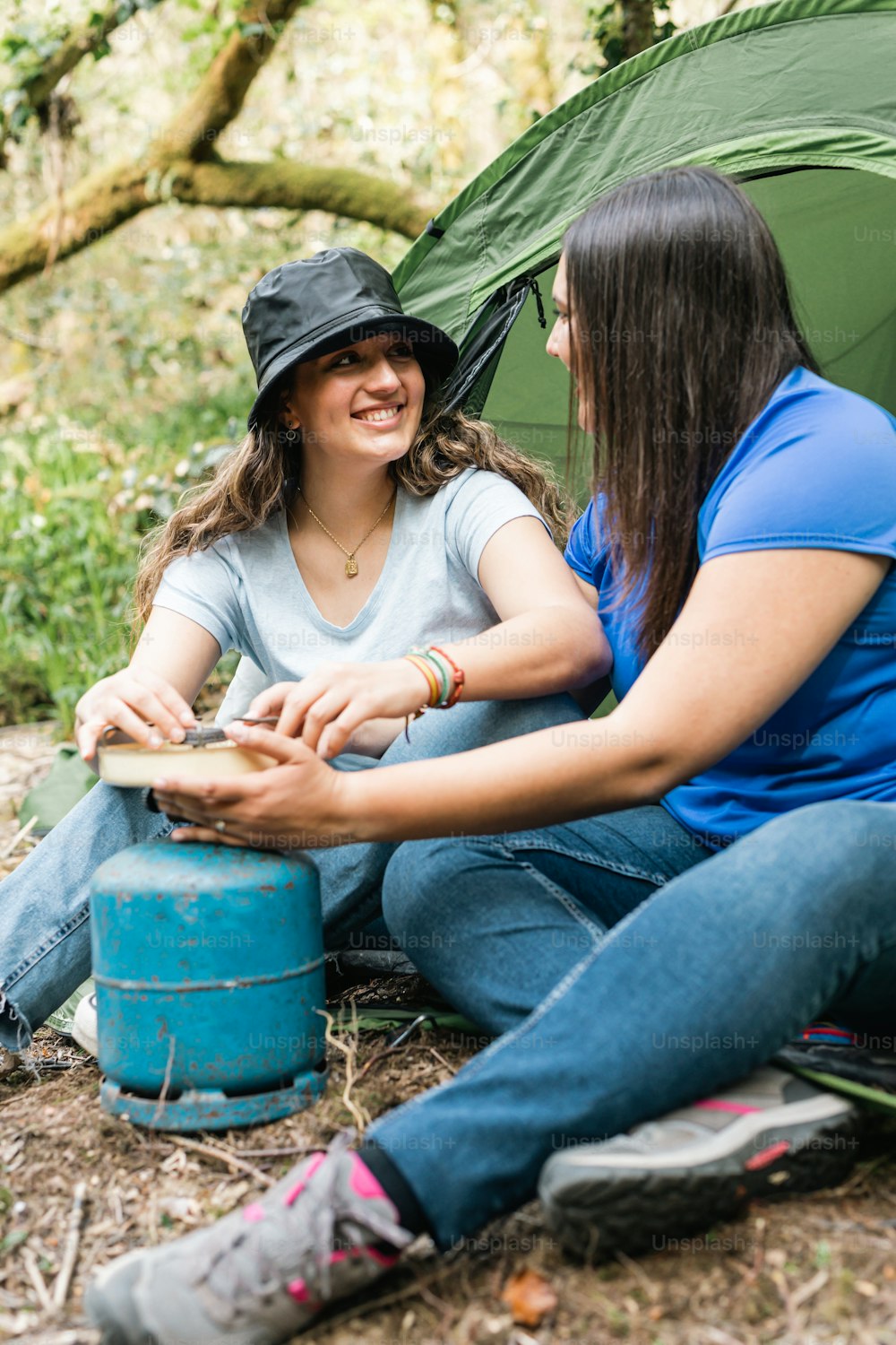 a couple of women sitting next to a green tent