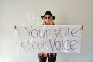 a woman holding a sign that says your vote is your voice