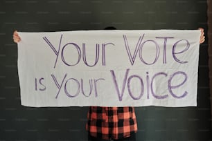 Una persona sosteniendo un cartel que dice que tu voto es tu voz