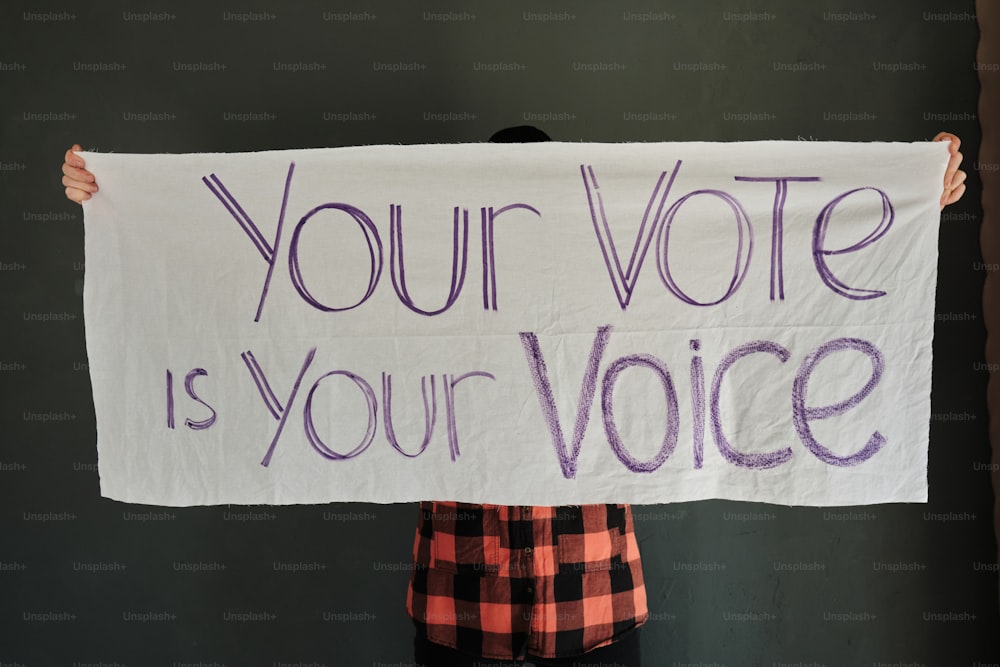 Una persona che tiene un cartello che dice che il tuo voto è la tua voce