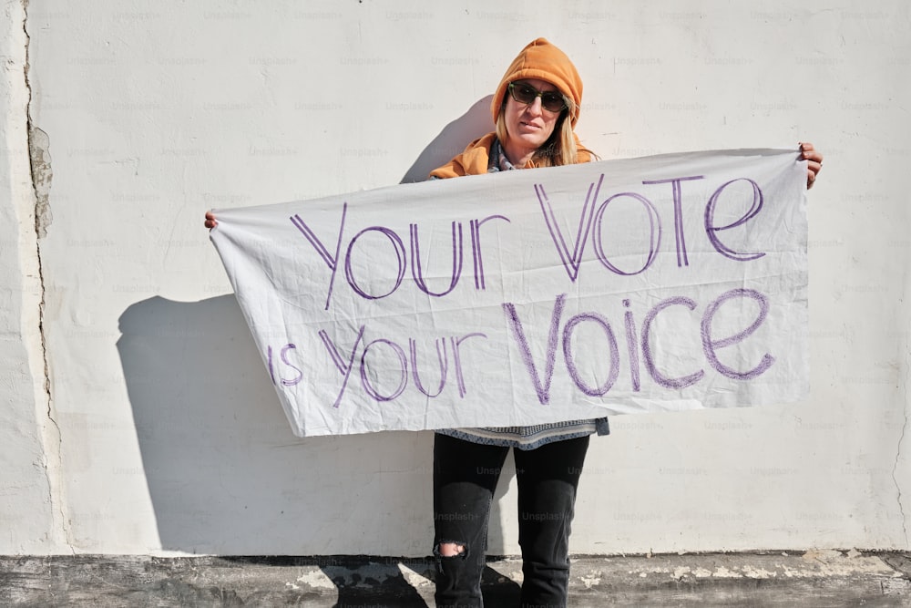 a woman holding a sign that says your vote is your voice
