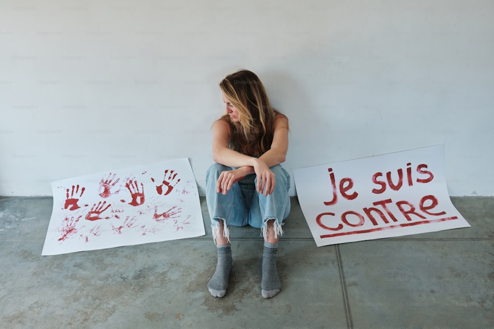Una mujer sentada en el suelo junto a dos carteles