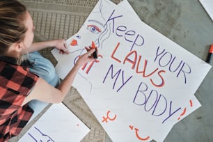 uma mulher está escrevendo em um sinal que diz manter suas leis em meu corpo