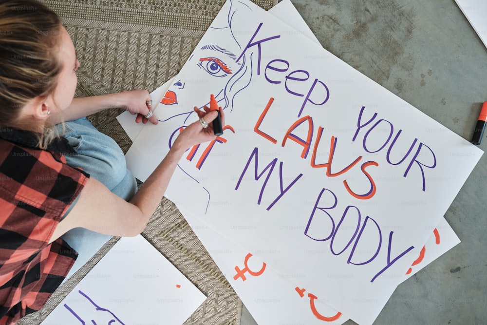 a woman is writing on a sign that says keep your laws in my body