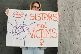 Una mujer sosteniendo un cartel que dice hermanas no víctimas
