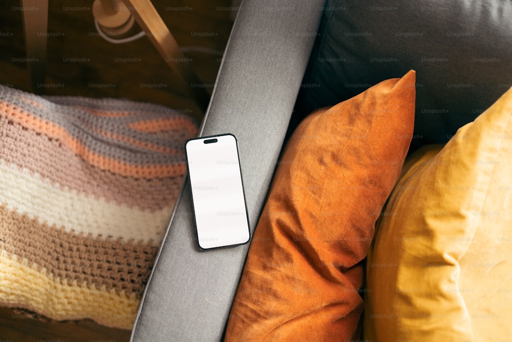 um telefone celular sentado em cima de um sofá ao lado de travesseiros