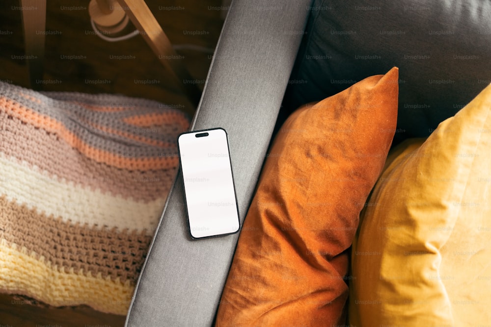 a cell phone sitting on top of a couch next to pillows