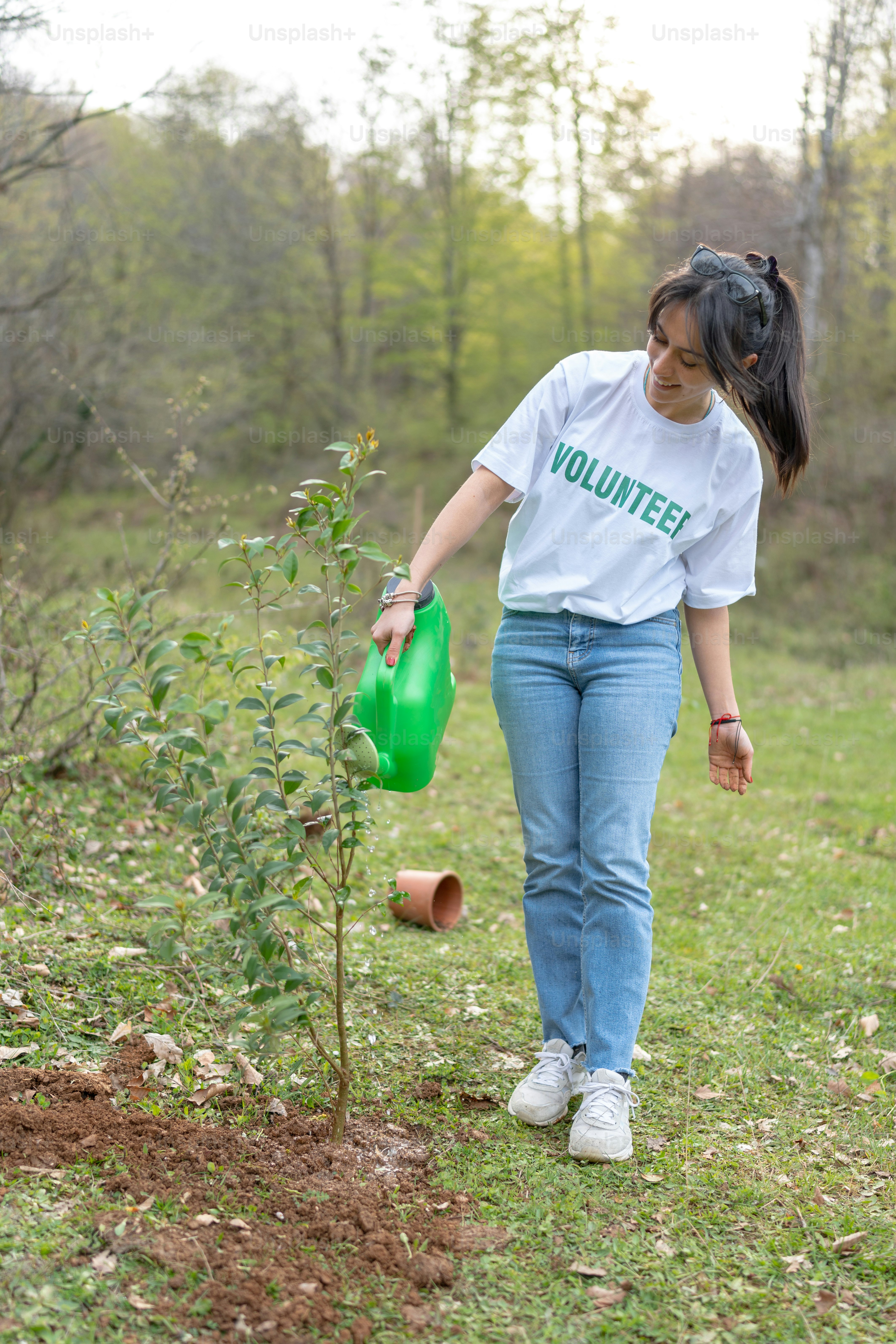 Une femme arrosant un arbre avec un arrosoir vert