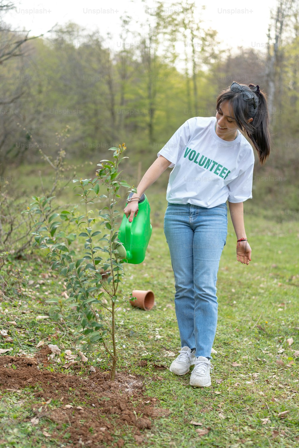 a woman watering a tree with a green watering can