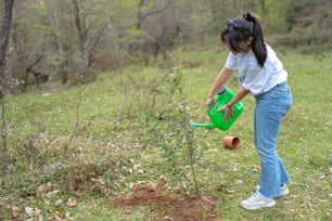 a woman watering a tree with a green watering can
