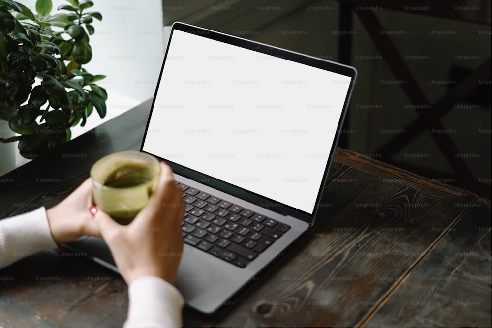 Una persona sosteniendo una taza de café frente a una computadora portátil