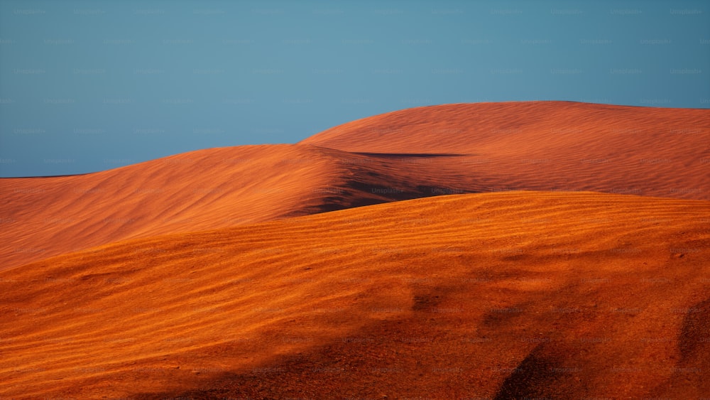 a group of sand dunes with a blue sky in the background