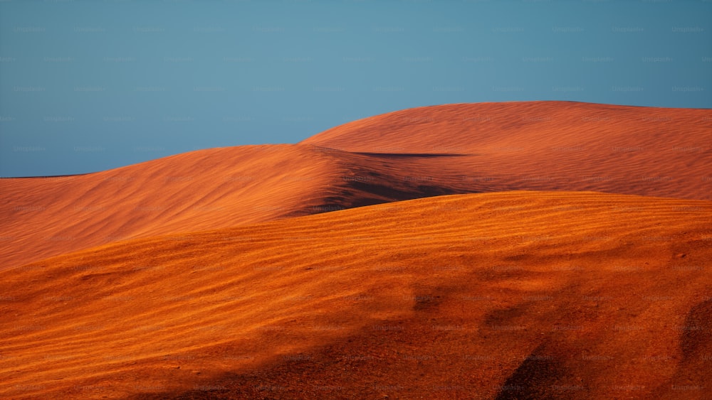 a group of sand dunes with a blue sky in the background