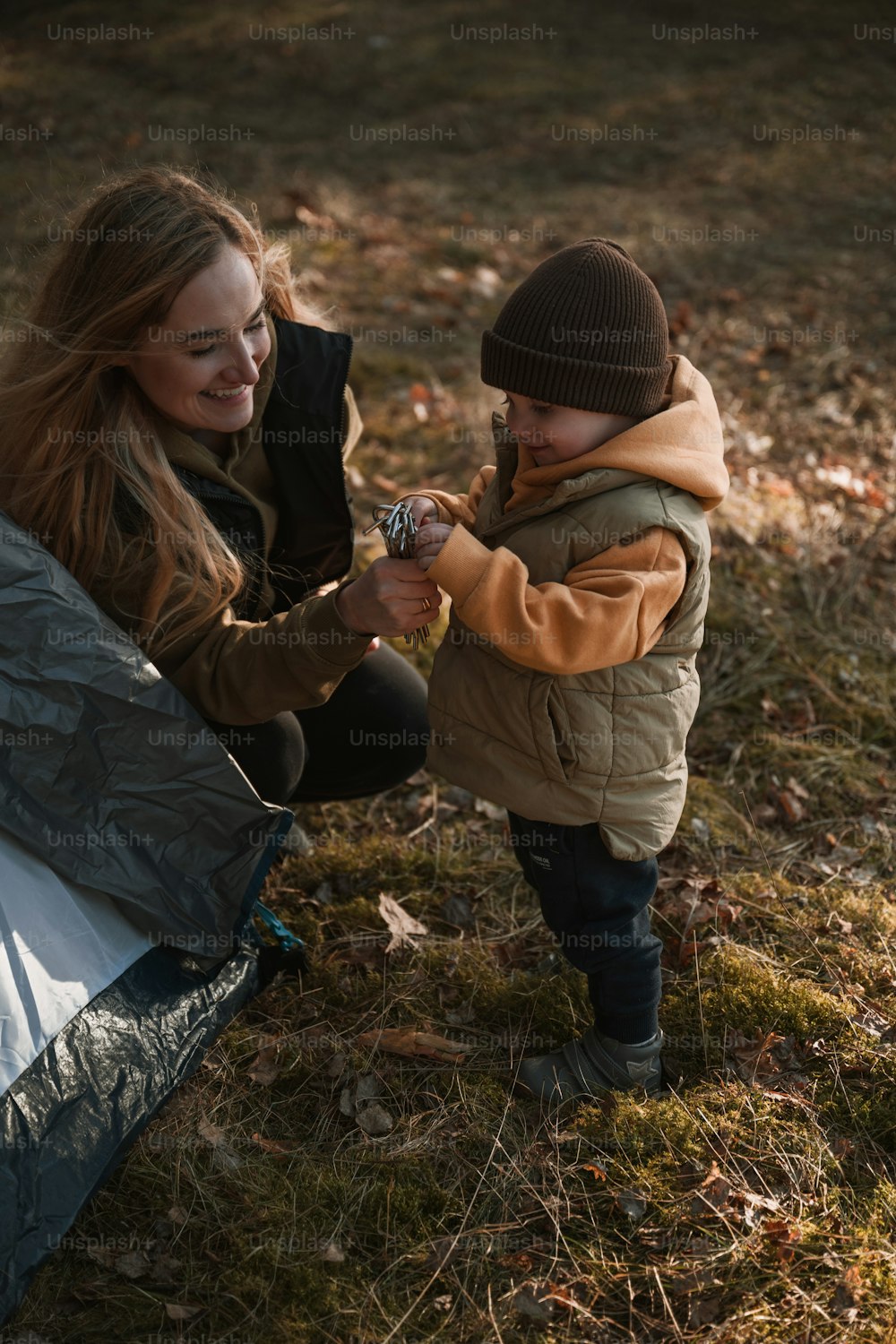 Una mujer sosteniendo la mano de un niño junto a una tienda de campaña
