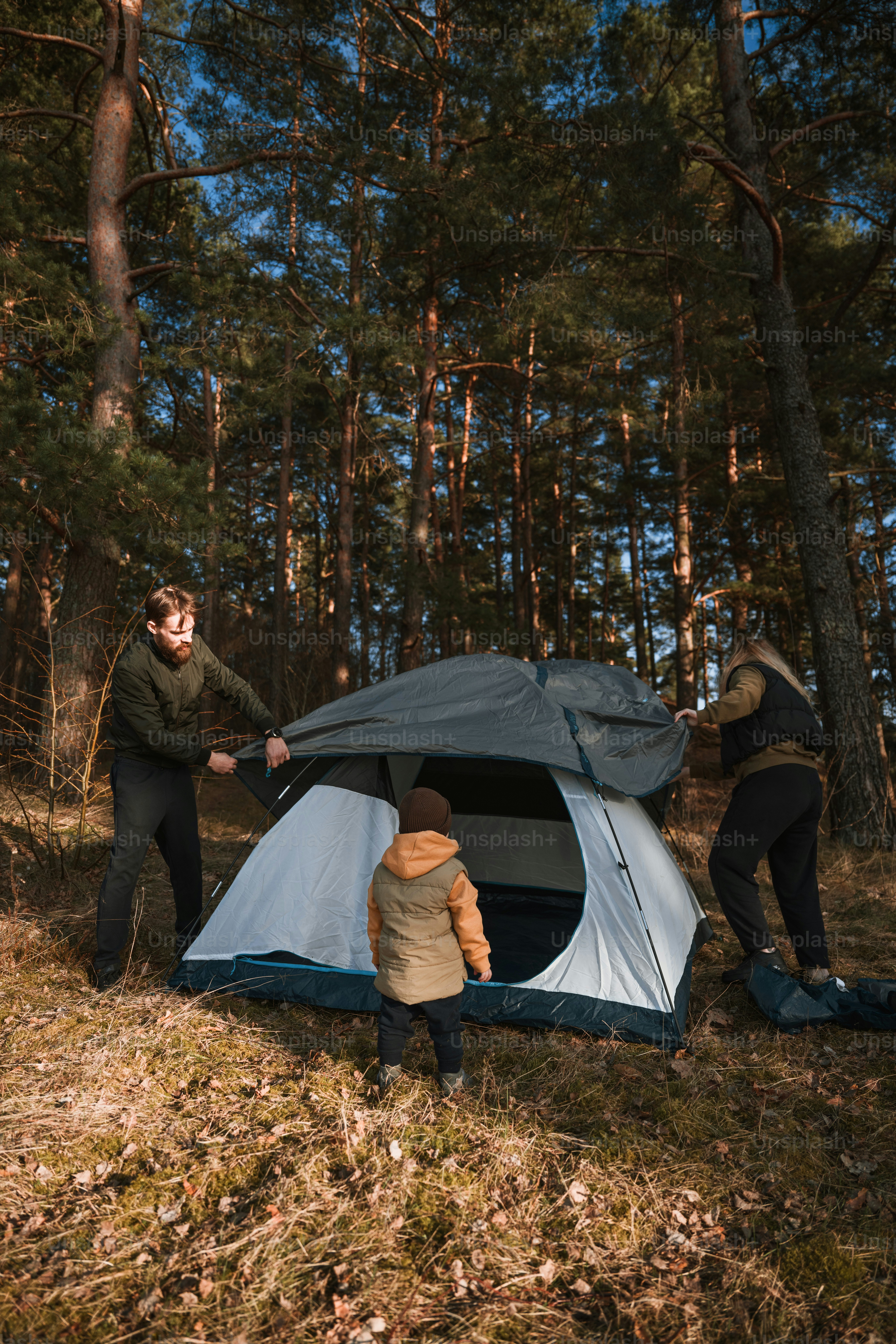 three people setting up a tent in the woods