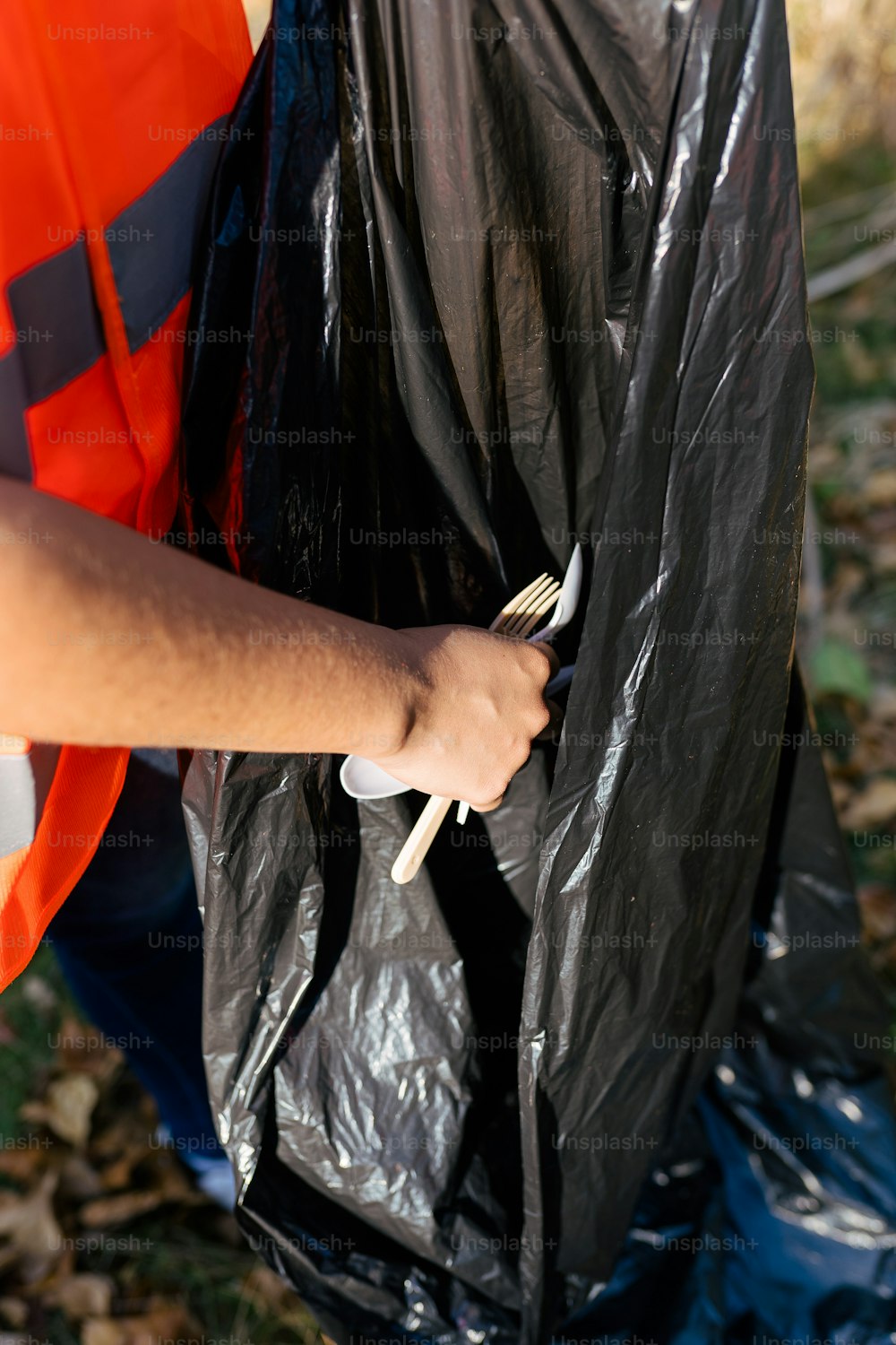 une personne vêtue d’un gilet orange tenant un sac en plastique noir