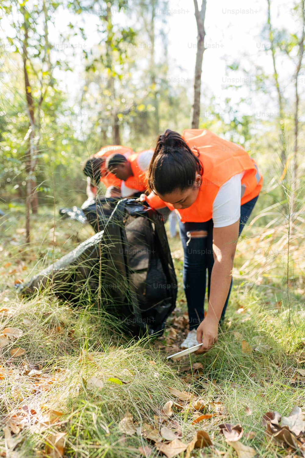 Una donna con un giubbotto arancione che raccoglie la spazzatura nel bosco