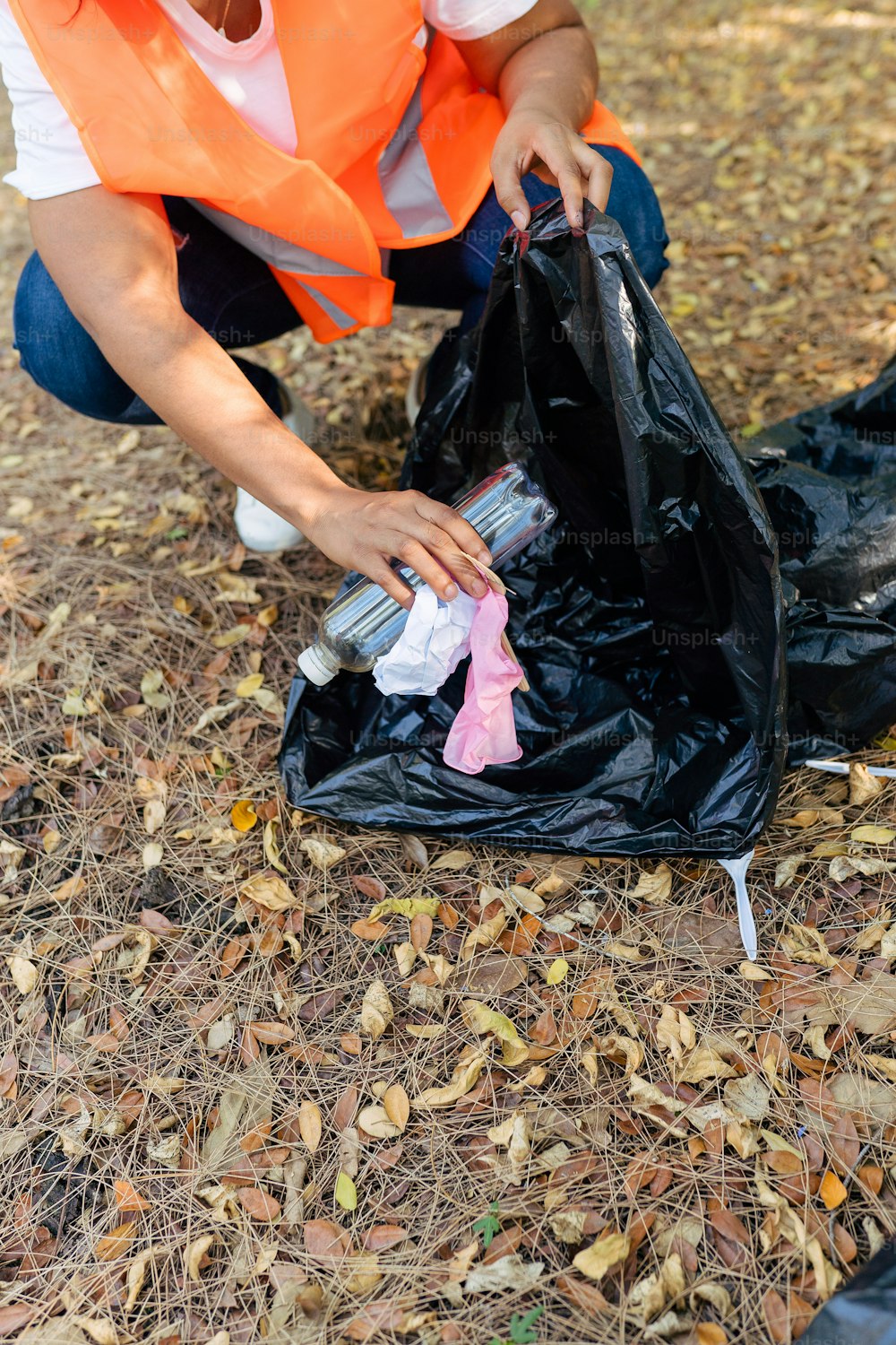Una donna con un giubbotto arancione sta raccogliendo la spazzatura