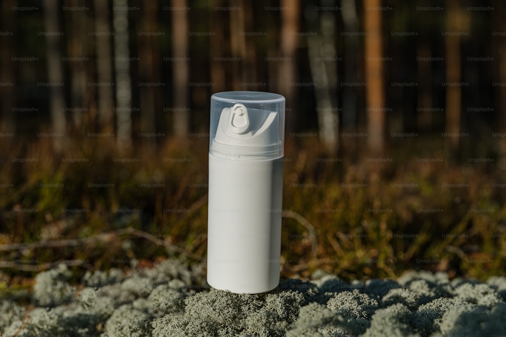 a white bottle sitting on top of a moss covered ground
