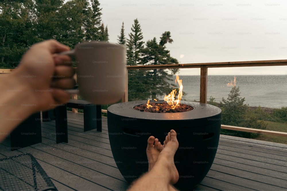 a person holding a coffee cup over a fire pit